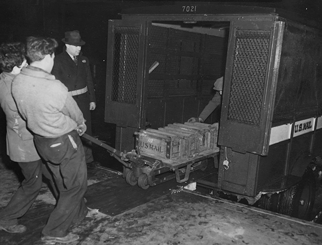 A black-and-white photograph of four men loading gold bullion into a shipping container.